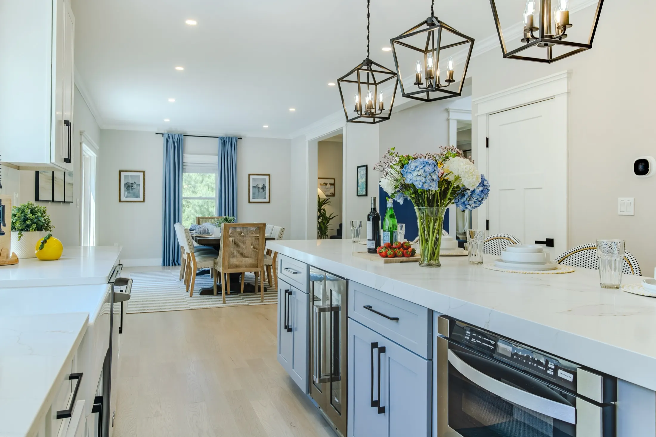 Kitchen with a long marble island, black lantern pendants, blue cabinetry, and the dining room beyond.